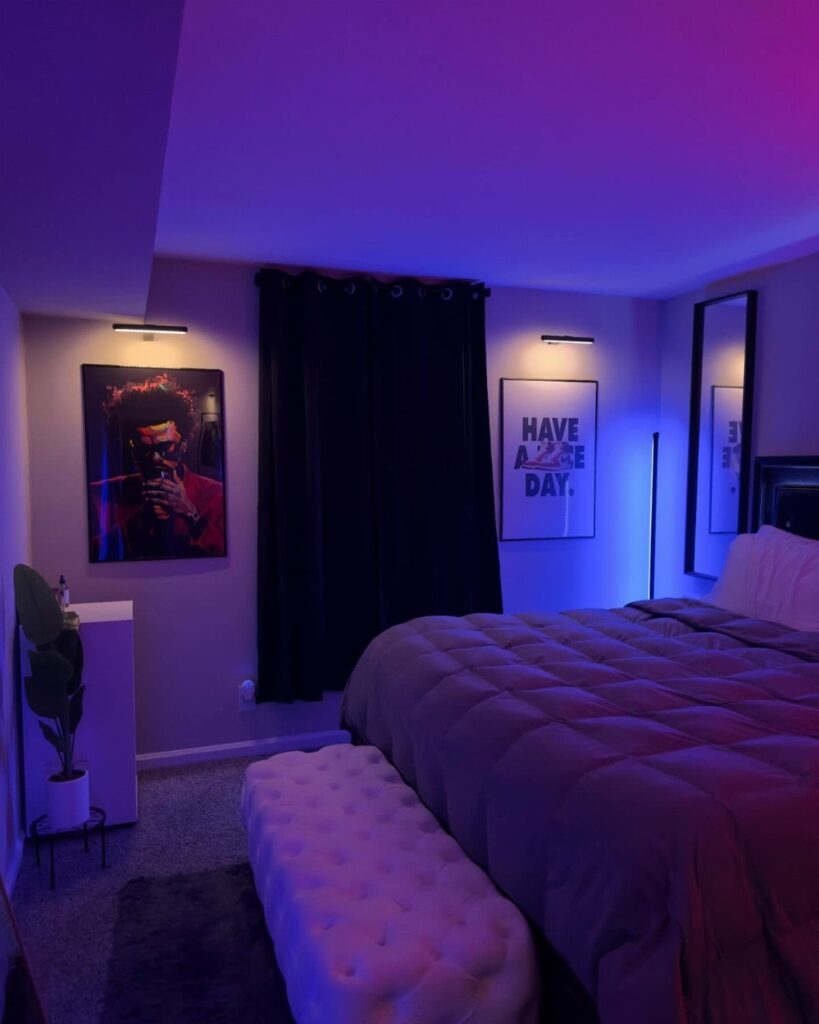 Bedroom with purple lighting, quilted bed, tufted bench, and wall art.