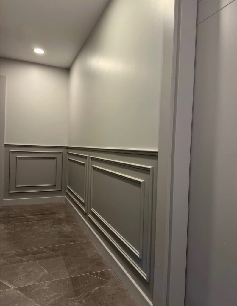 Grey hallway walls with decorative chair rail and wainscoting panels over marble floors.