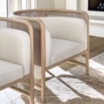 Two white armchairs with wooden frames and cane detailing on a beige rug.