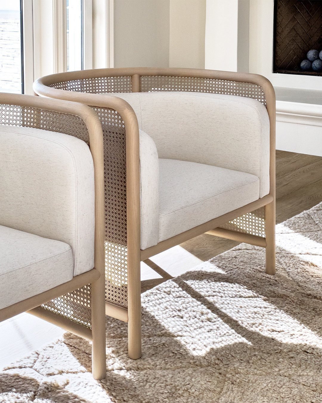 Two white armchairs with wooden frames and cane detailing on a beige rug.