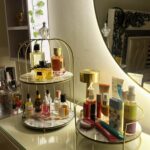 Gold metal trays with marble bases holding perfumes and skincare on a white dresser.