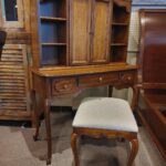Wooden secretary desk with hutch and matching upholstered stool in a furniture store