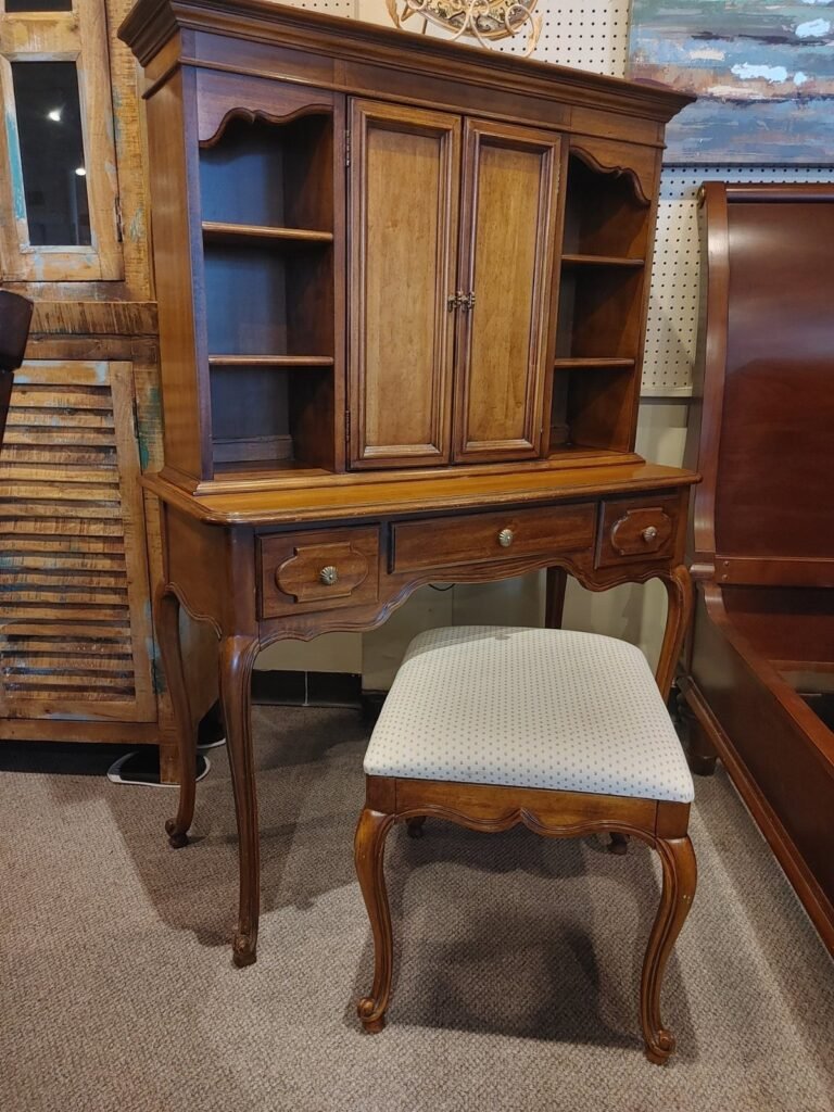 Wooden secretary desk with hutch and matching upholstered stool in a furniture store