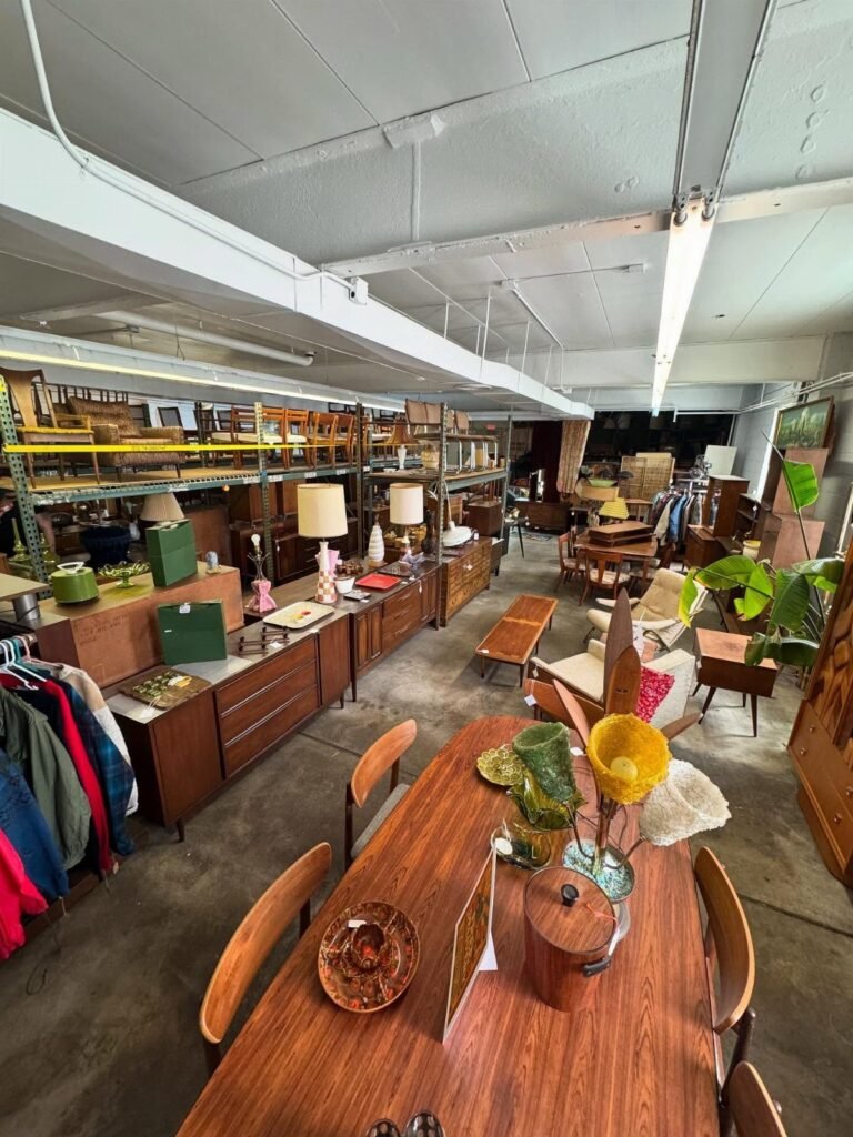 Mid-century modern wooden furniture displayed in a spacious industrial warehouse showroom.