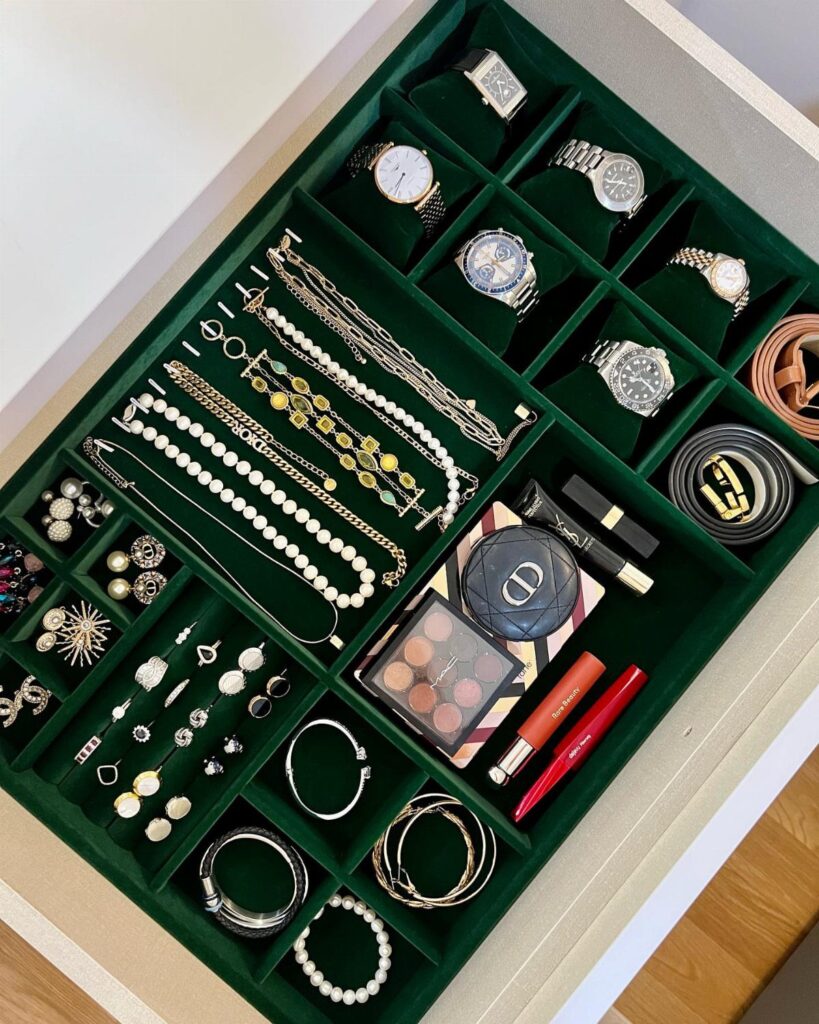 Green velvet jewelry tray in a drawer holding watches, necklaces, and makeup.