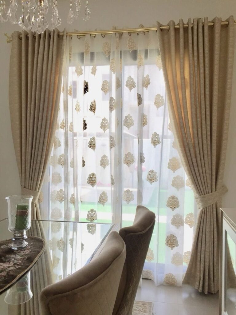 Beige pleated curtains and gold patterned sheer curtains in a bright living room.