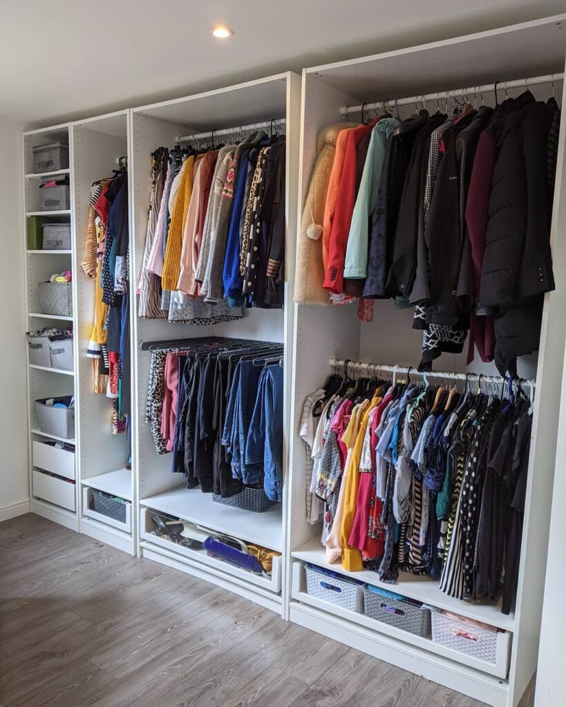 White open closet system with hanging clothes and storage bins on grey flooring