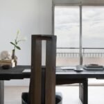 Dark wooden dining table and high-back chair in a minimalist white interior room