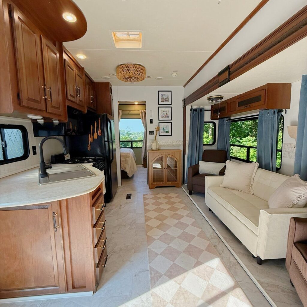 RV interior with wooden cabinetry, white sofa, blue curtains, and a patterned rug.