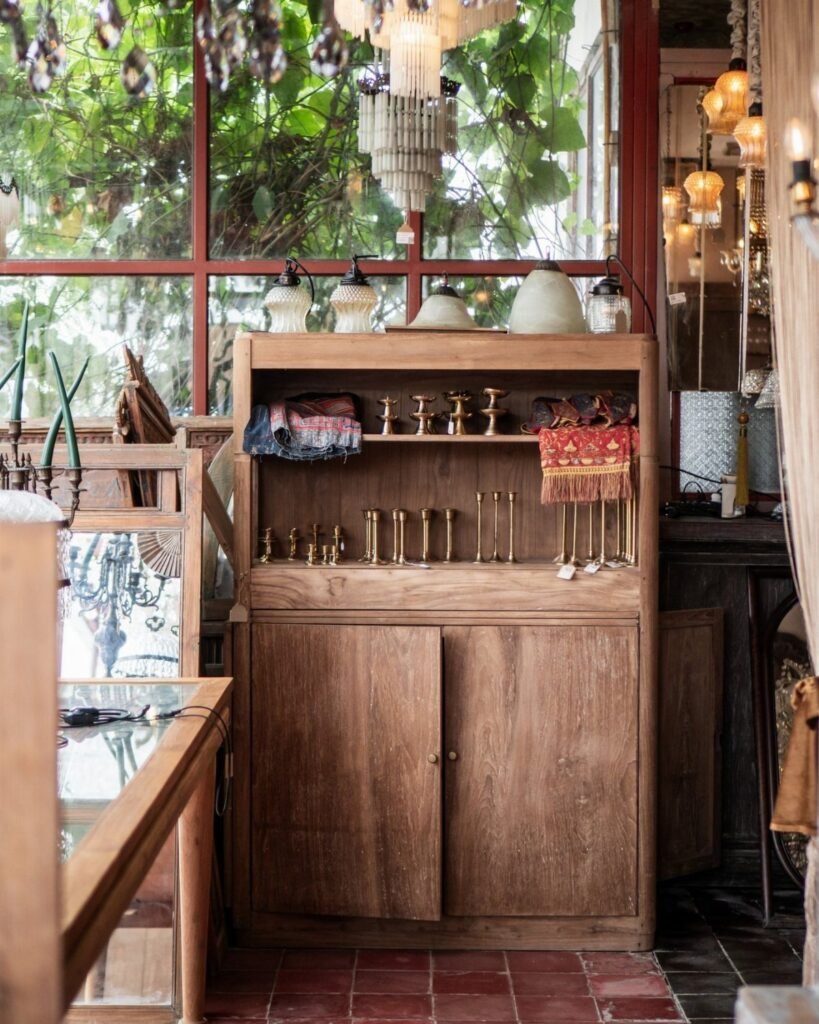 Wooden vintage hutch displaying brass candlesticks and textiles in a bright boutique setting